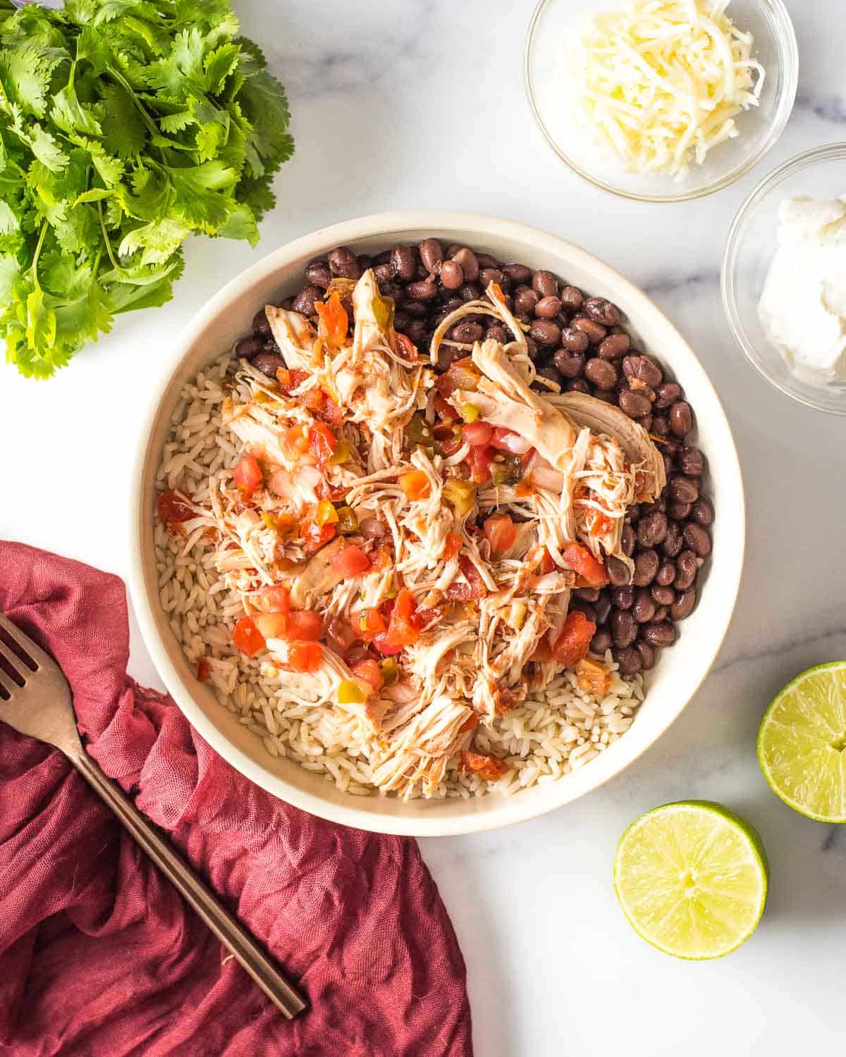 A bowl of slow cooker salsa chicken, mexican rice, black beans and limes.