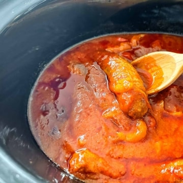 A crock pot filled with sausages, peppers and marinara sauce.