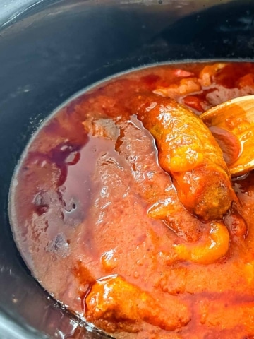 A crock pot filled with sausages, peppers and marinara sauce.