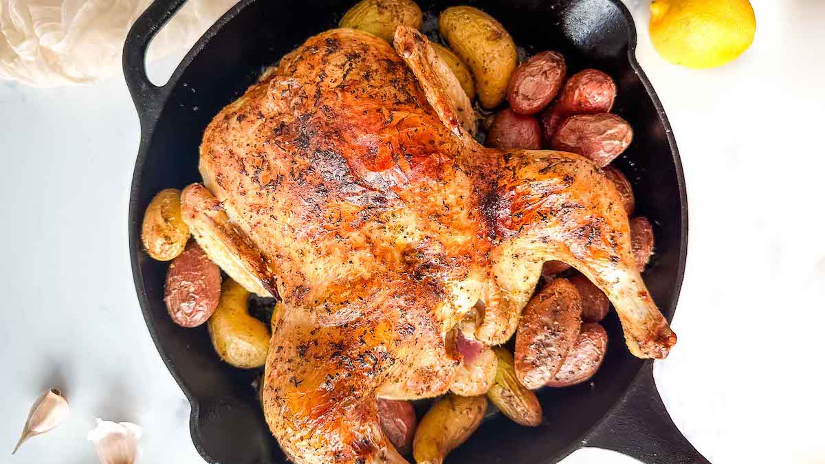 A roasted chicken with potatoes in a cast iron skillet.