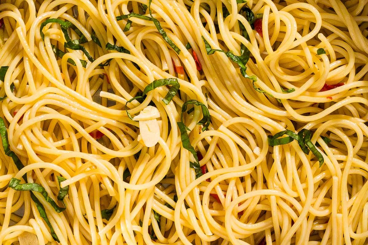 A close up of a bowl of spaghetti with garlic, chilis, and basil.