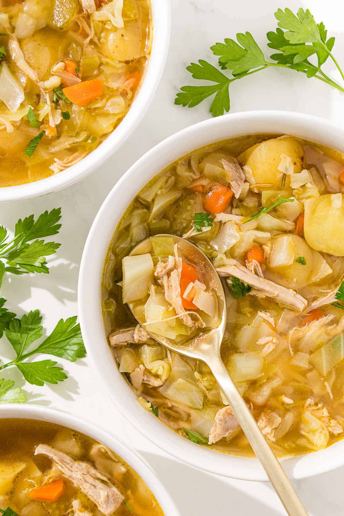 Three bowls of chicken and cabbage soup with a spoon.