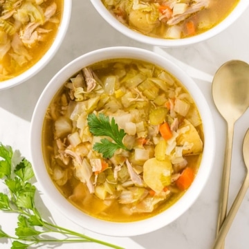 Three bowls of chicken cabbage soup with parsley.