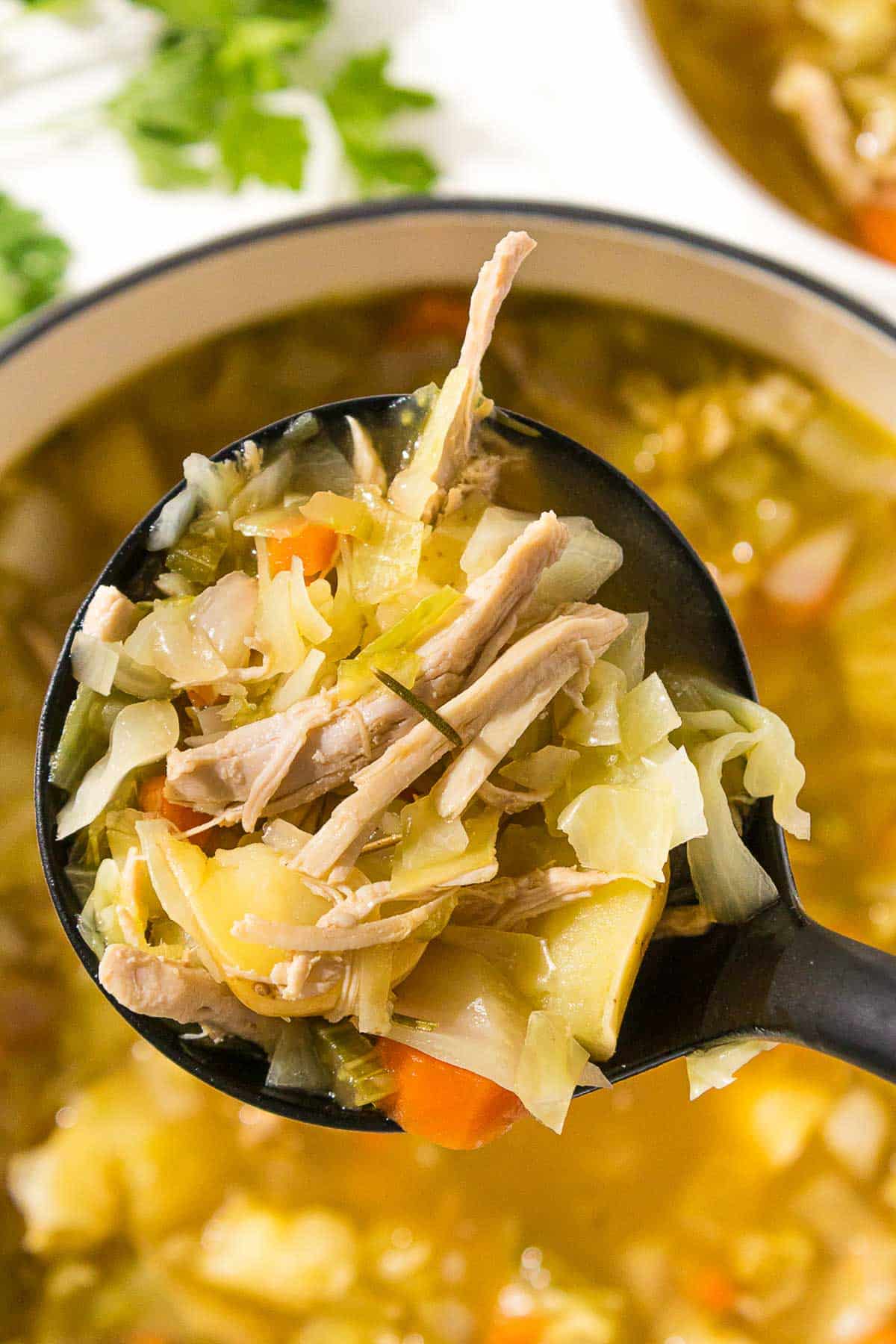 Chicken soup with cabbage and carrots in a black ladel.