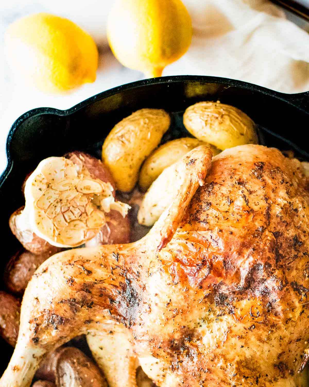 A chicken in a cast iron skillet with potatoes and lemons.