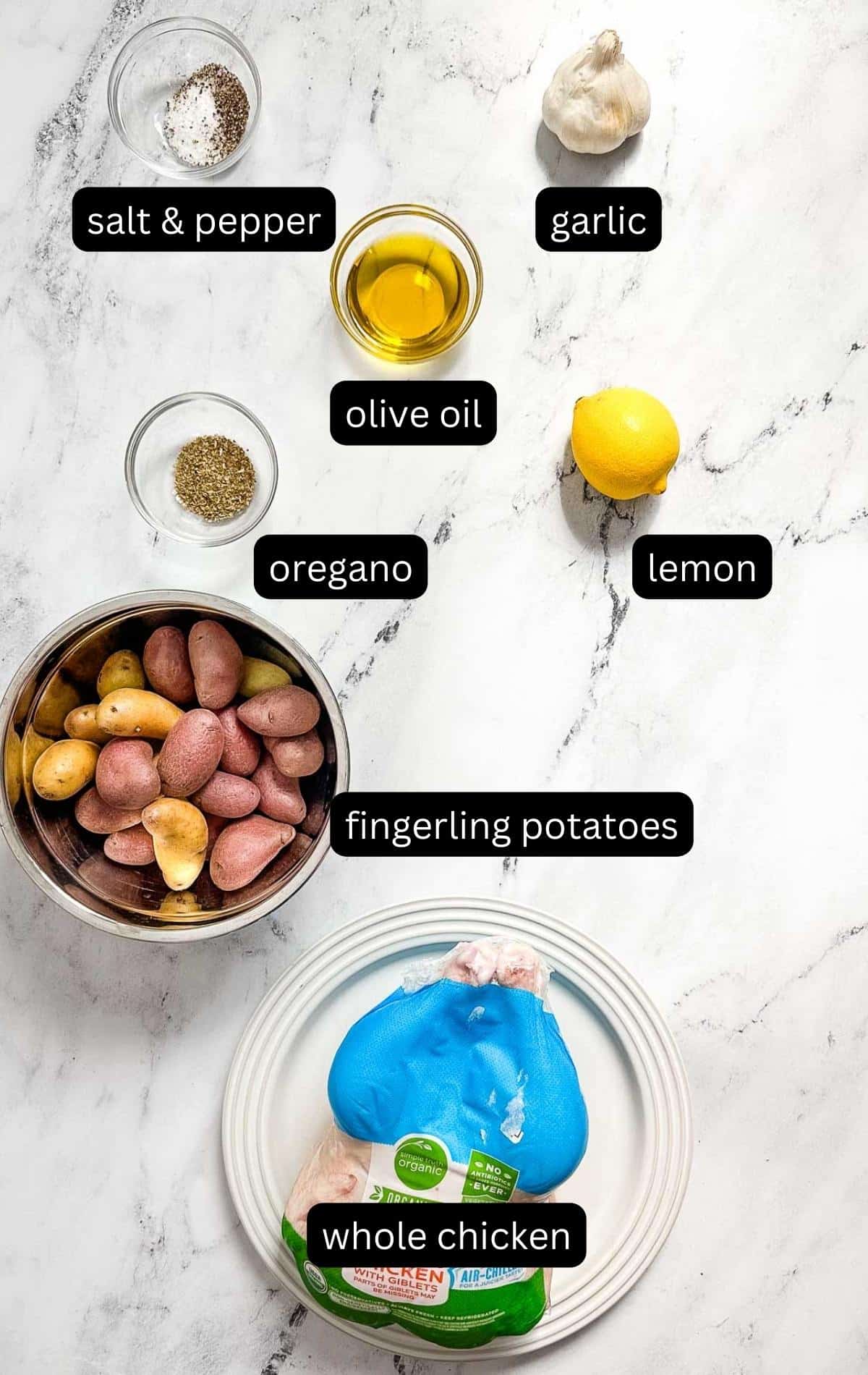 Labeled ingredients for Greek roast chicken on a marble table.