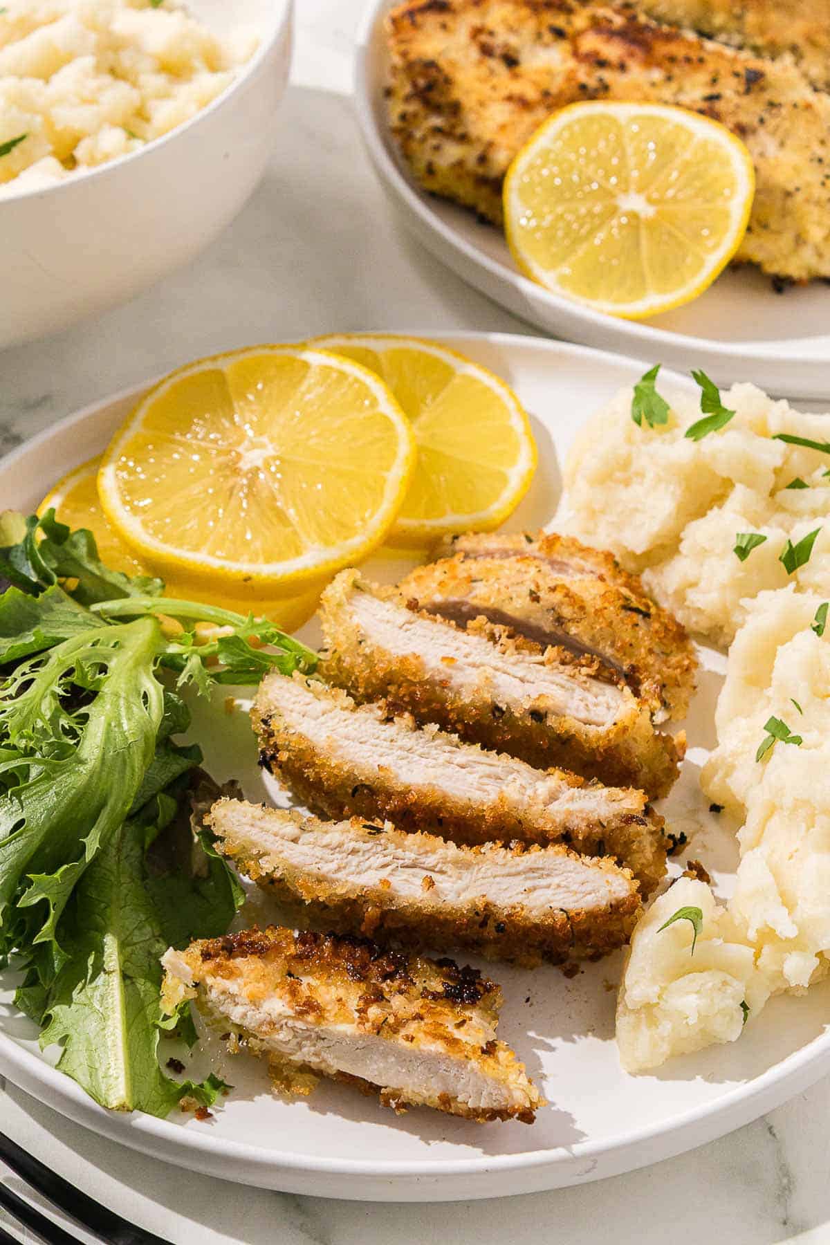 A plate with Italian chicken cutlets, salad, mashed potatoes and lemons.