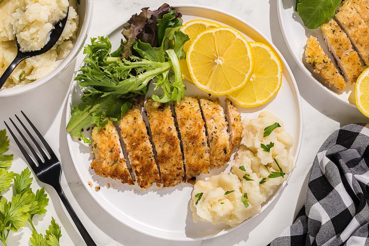 A plate with Italian chicken cutlets, salad, mashed potatoes and lemons.