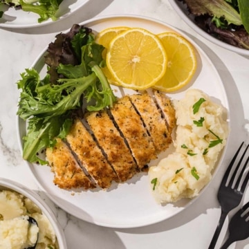 A plate of chicken cutlets with mashed potatoes and lemons.