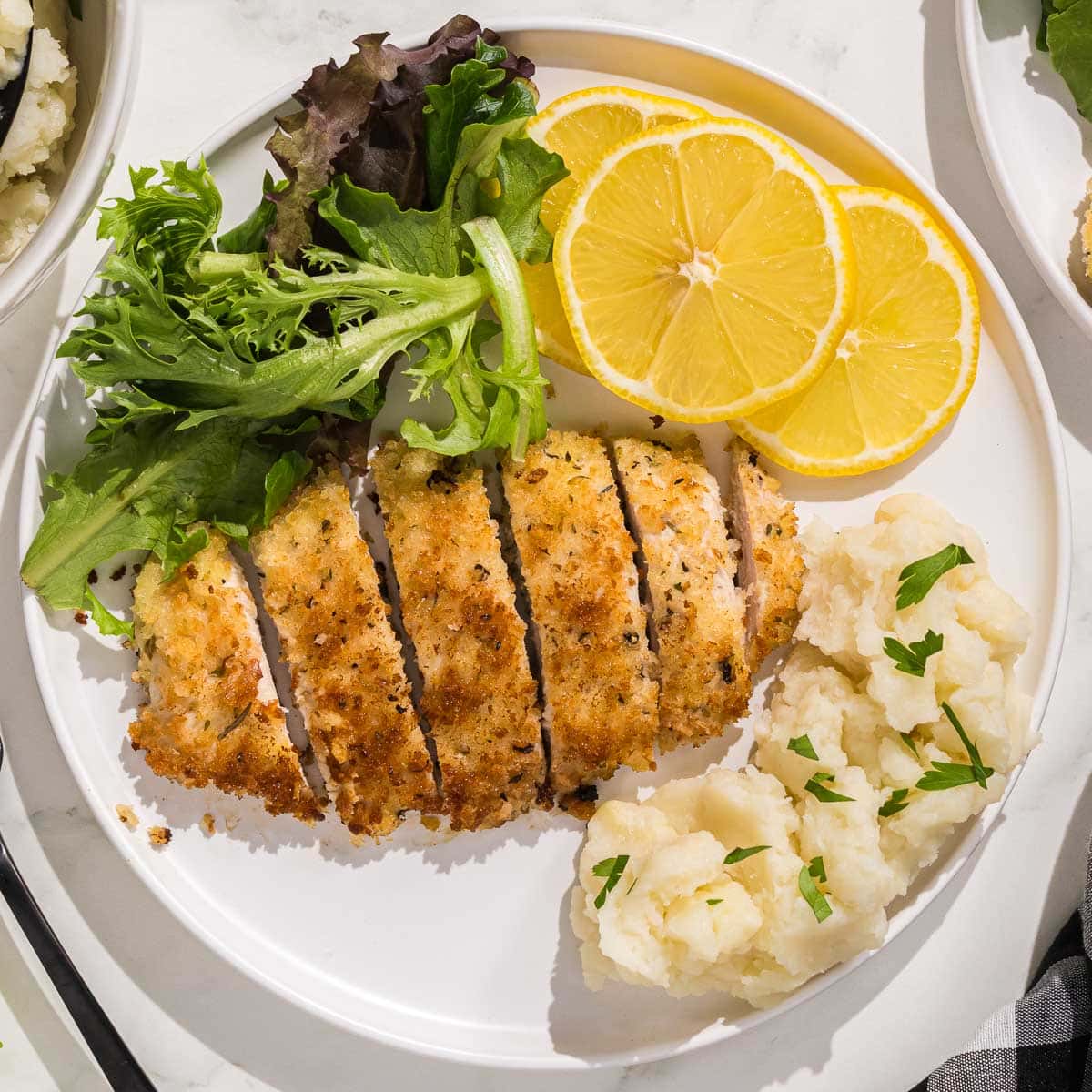 A plate of Italian chicken cutlets, mashed potatoes and lemons.