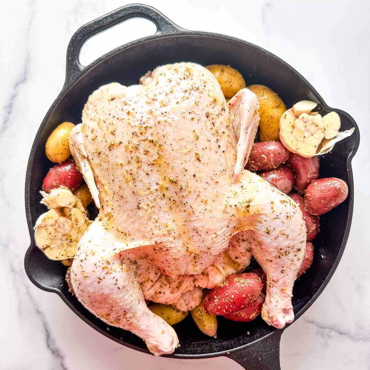 A chicken and potatoes in a cast iron skillet.