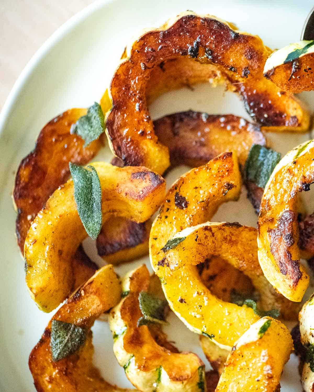 Roasted delicata squash with sage leaves on a plate.
