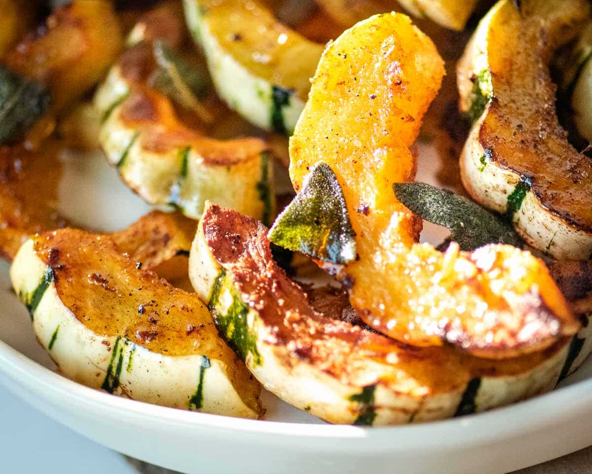 Roasted delicata squash with sage in a white bowl.