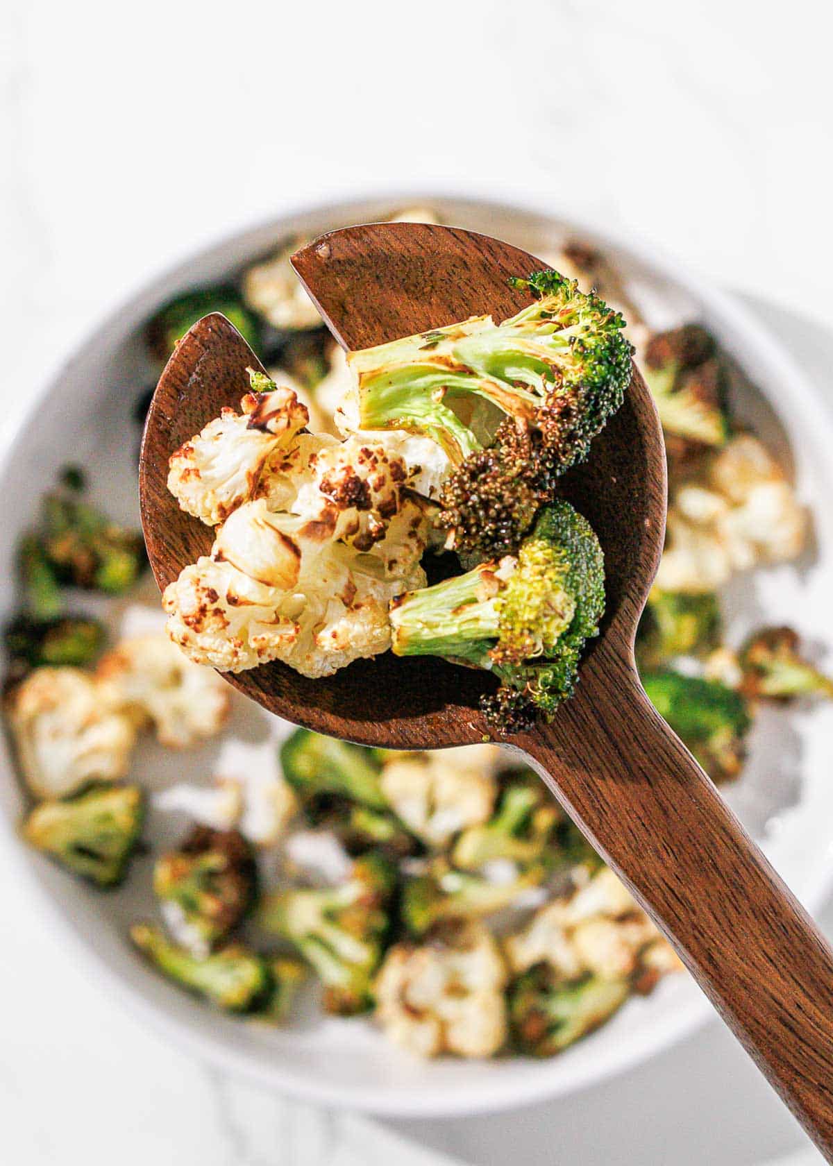 Air fryer broccoli and cauliflower on a wooden spoon.