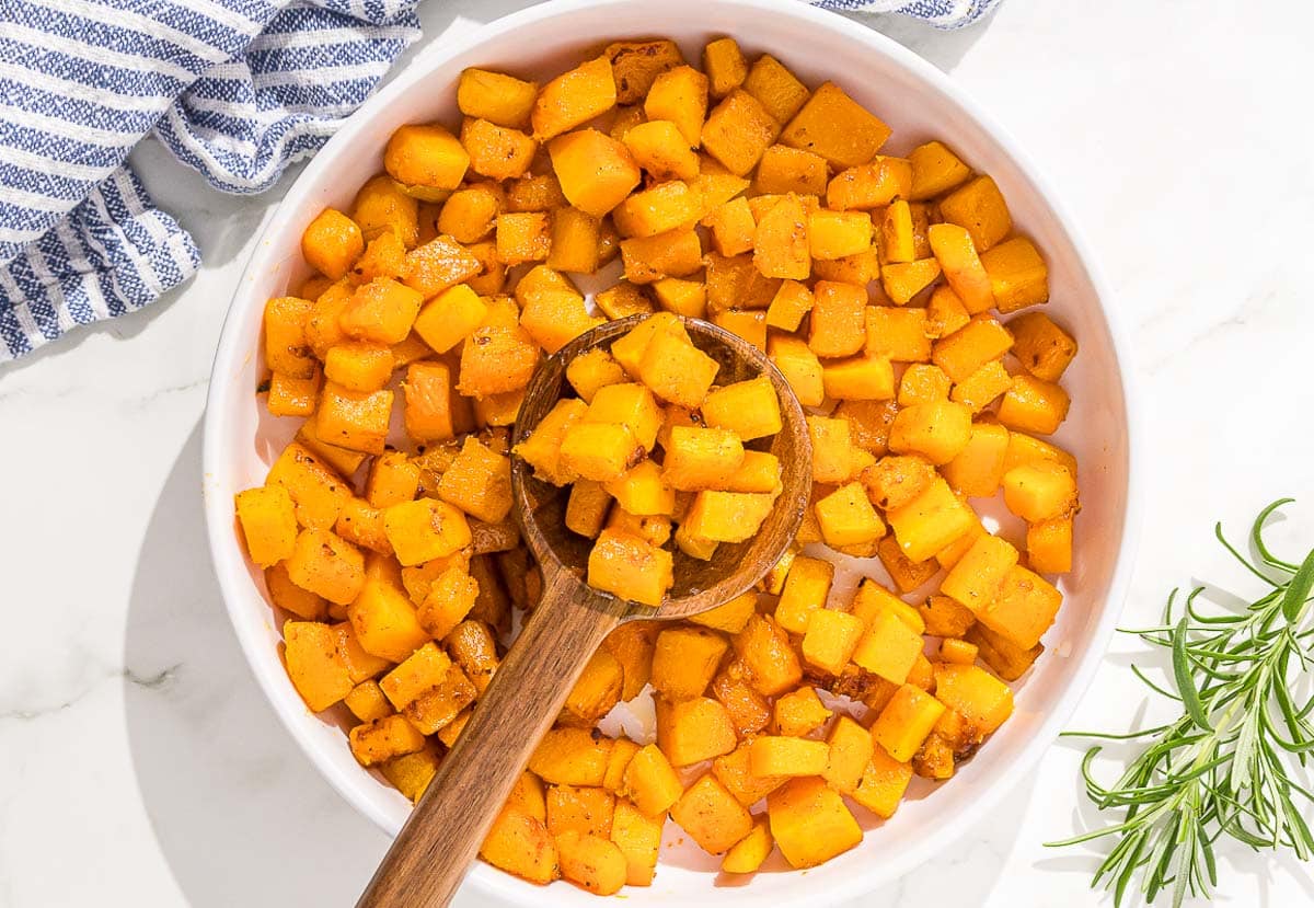 Sautéed butternut squash in a white bowl with a wooden spoon.