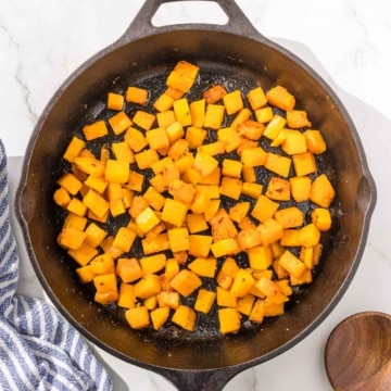 Cubed butternut squash in a skillet on a marble countertop.