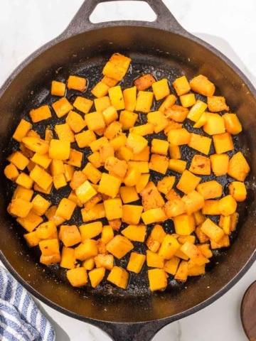 Cubed butternut squash in a skillet on a marble countertop.