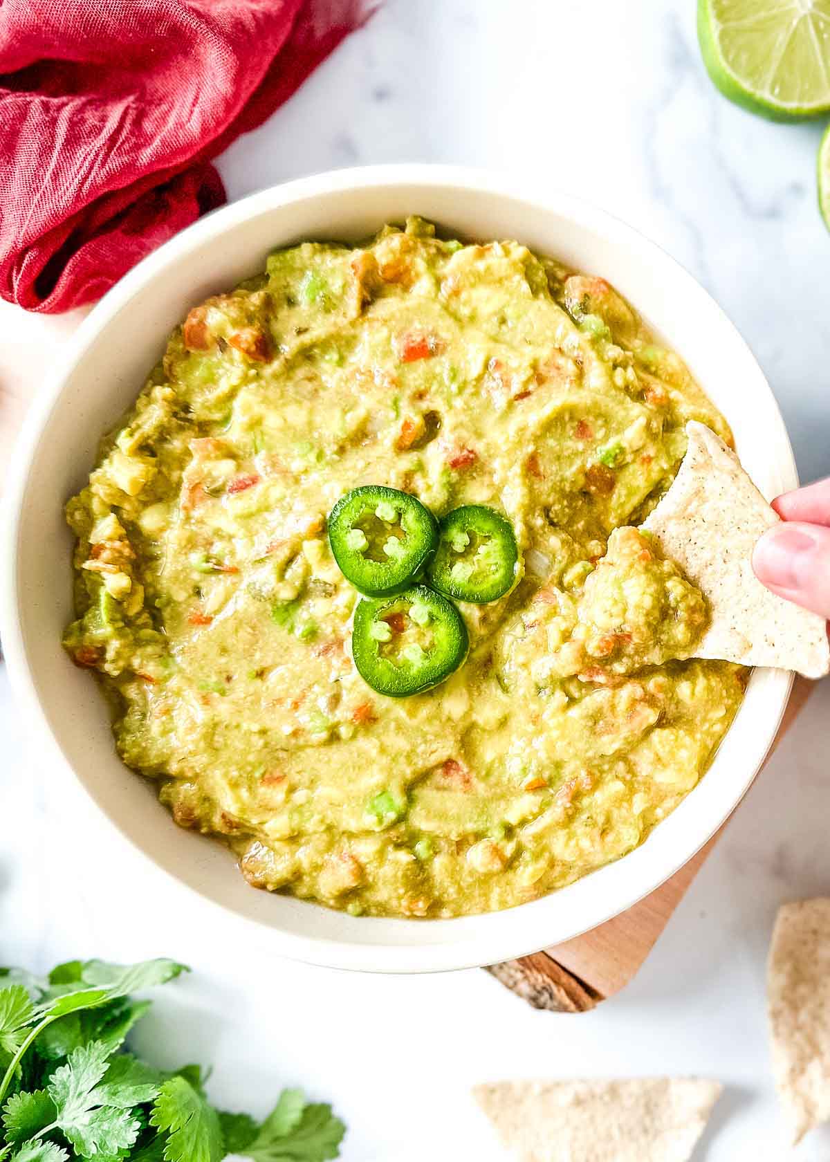 Guacamole dip in a white bowl with a hand holding a tortilla chip.