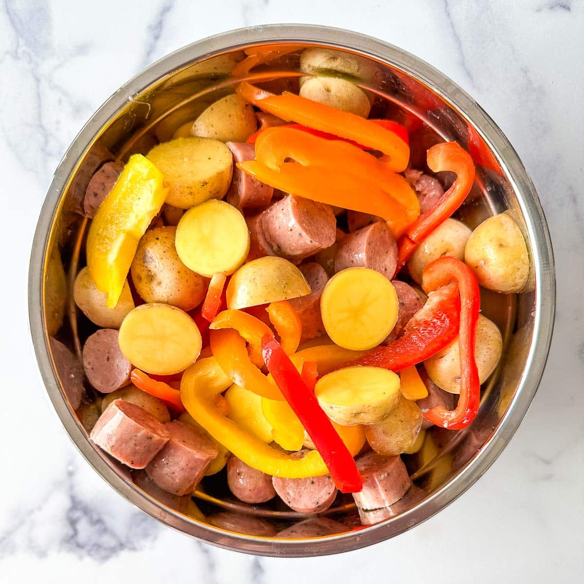 A bowl full of peppers, potatoes, and sausages tossed in olive oil.
