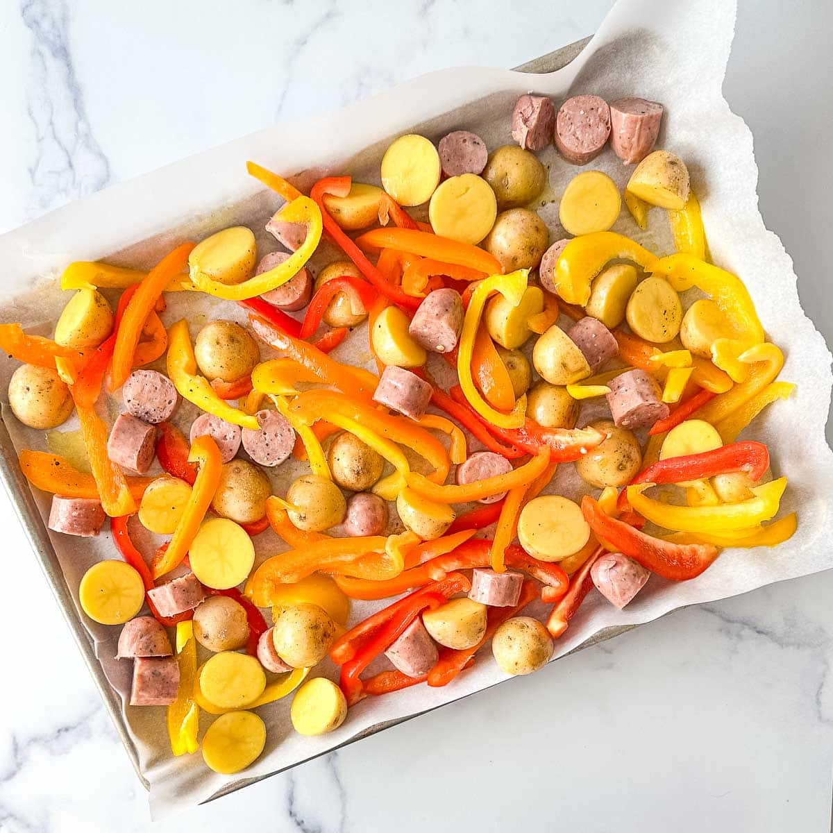 A baking sheet filled with peppers, potatoes, and sliced chicken sausages.