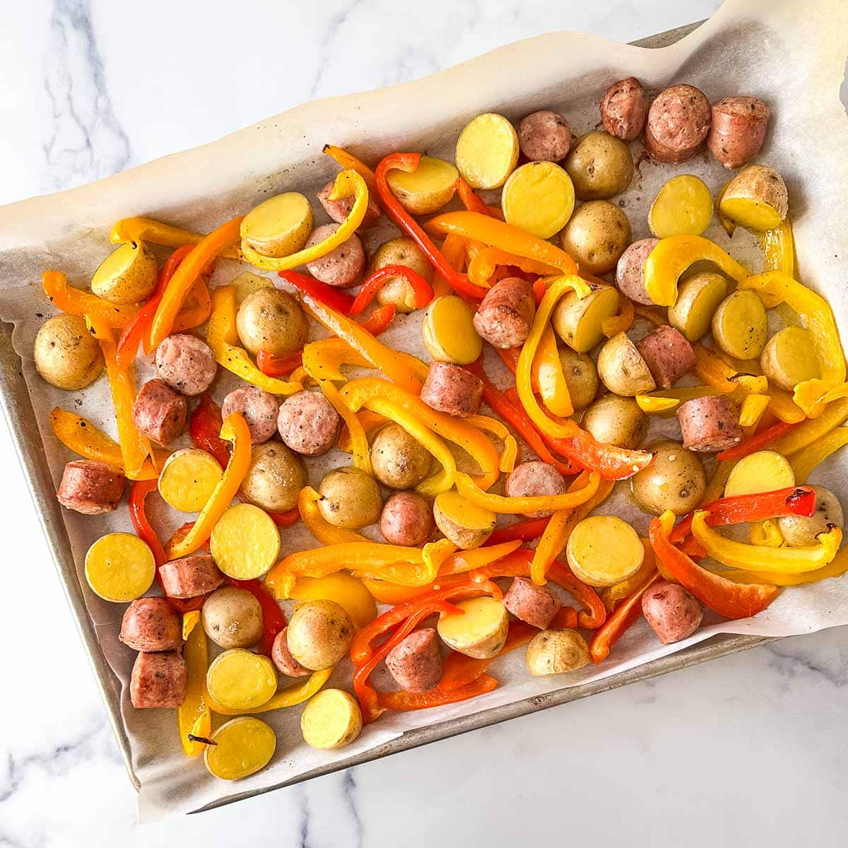 A baking sheet filled with roasted vegetables, potatoes and chicken sausages.