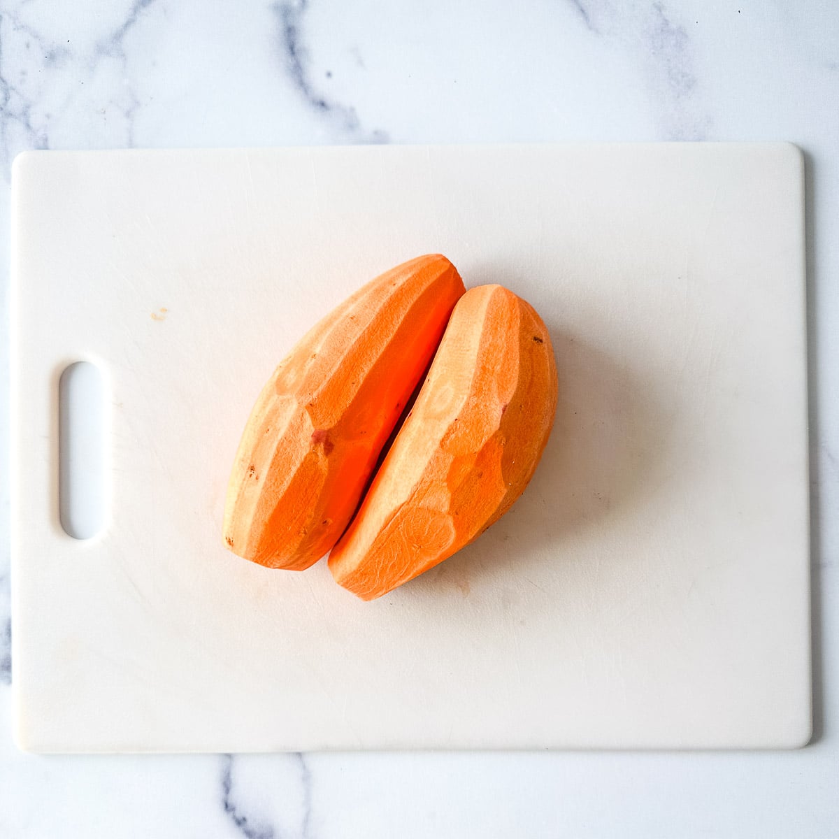 Two peeled sweet potatoes on a cutting board.