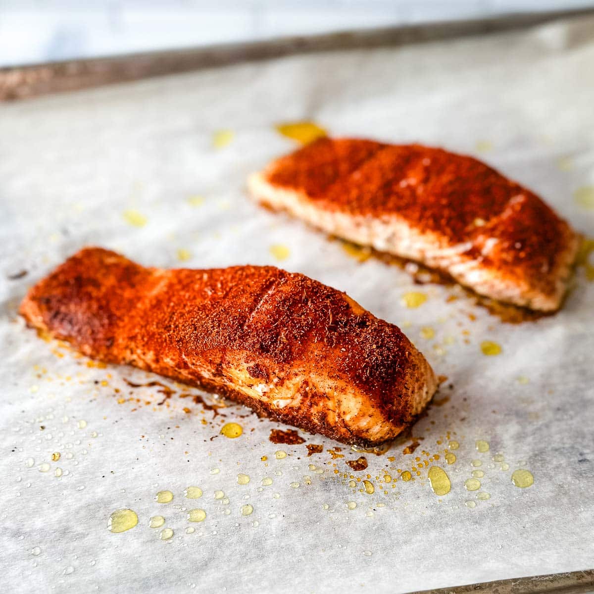 Two baked blackened salmon fillets on a baking sheet.