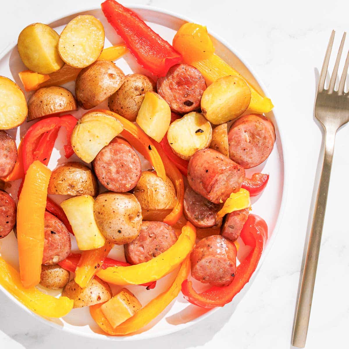 A plate with chicken sausage, potatoes and bell peppers on it.