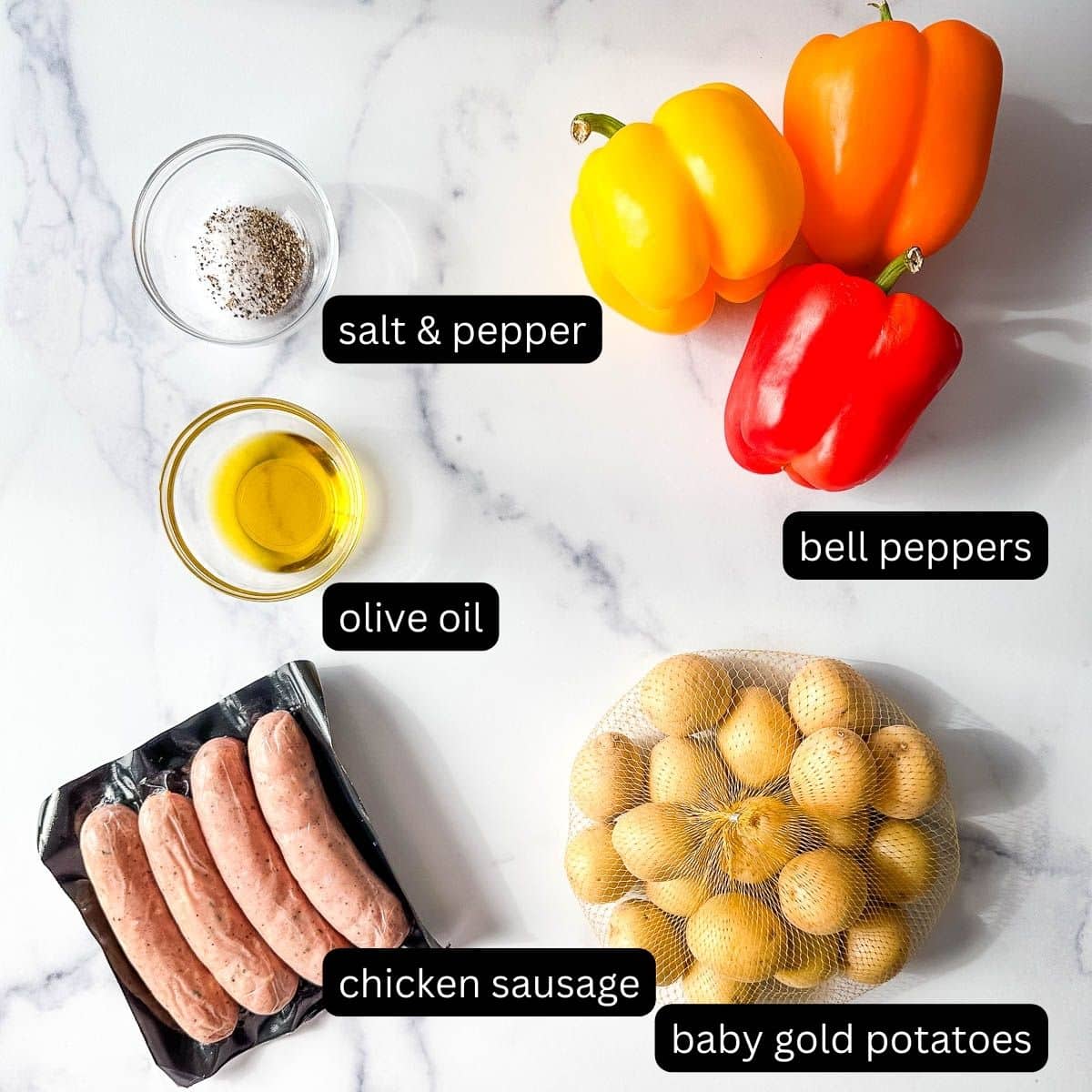 The ingredients for a recipe for sausage and potatoes on a marble table.
