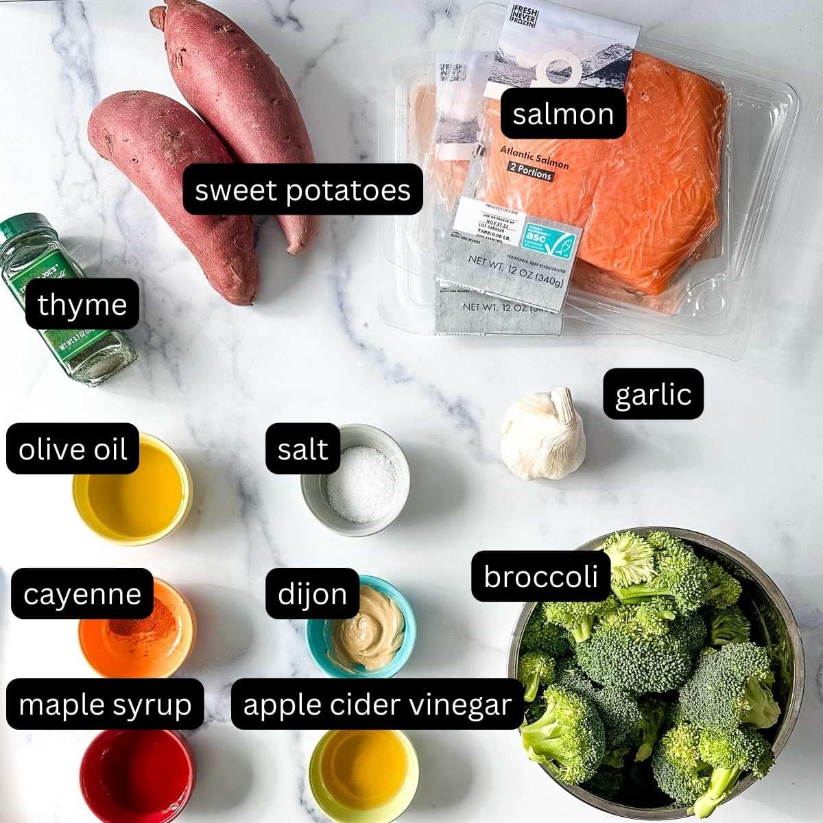 The labeled ingredients for maple dijon salmon and veggies on a white marble counter.