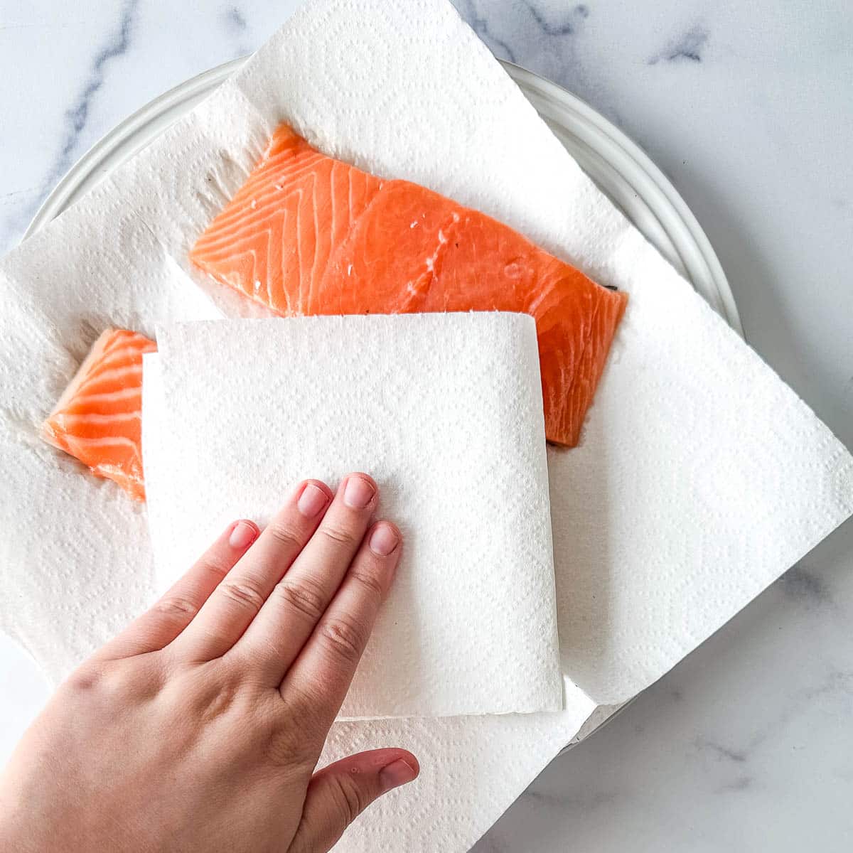 A person patting salmon dry with paper towels.