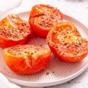 Four sliced and air-fried tomatoes on a plate with spices.