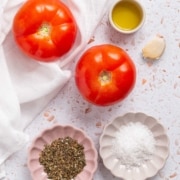 A plate with tomatoes, garlic, thyme, olive oil and salt on a white background.