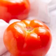 Two tomatoes on top of a white cloth.