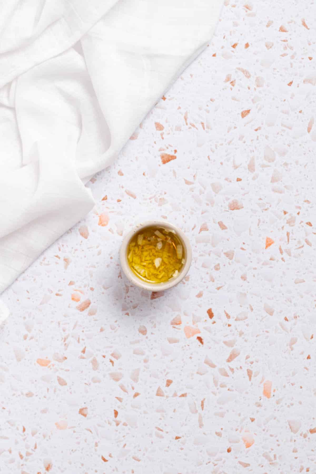 A bowl of olive oil and garlic and a white towel on a white background.
