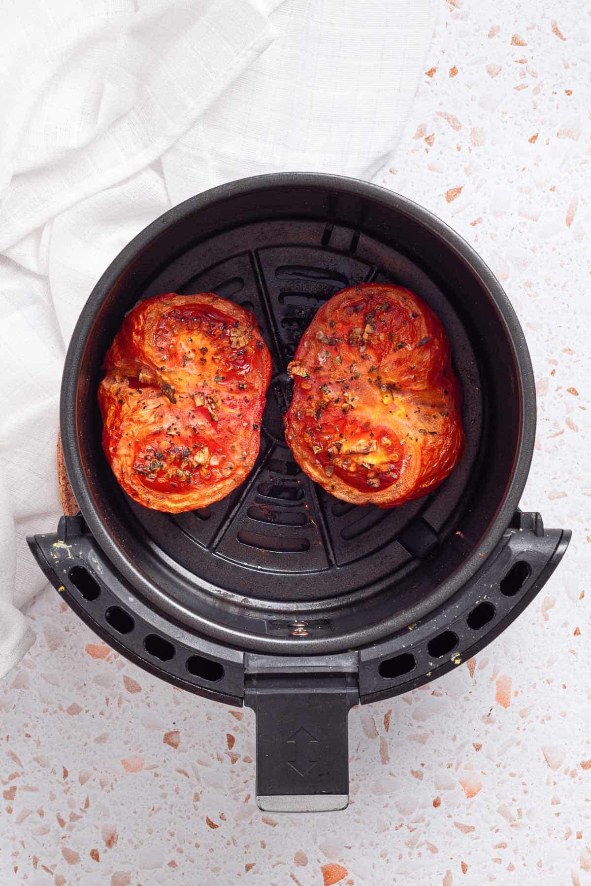 Two tomatoes in an air fryer.