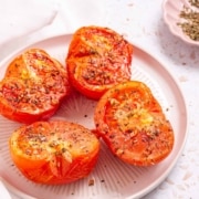 Halved air fryer tomatoes on a plate with herbs and spices.