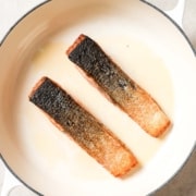 Two pieces of salmon being cooked in a pan skin-side up.