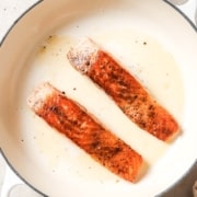 Two salmon fillets are being cooked in a skillet.
