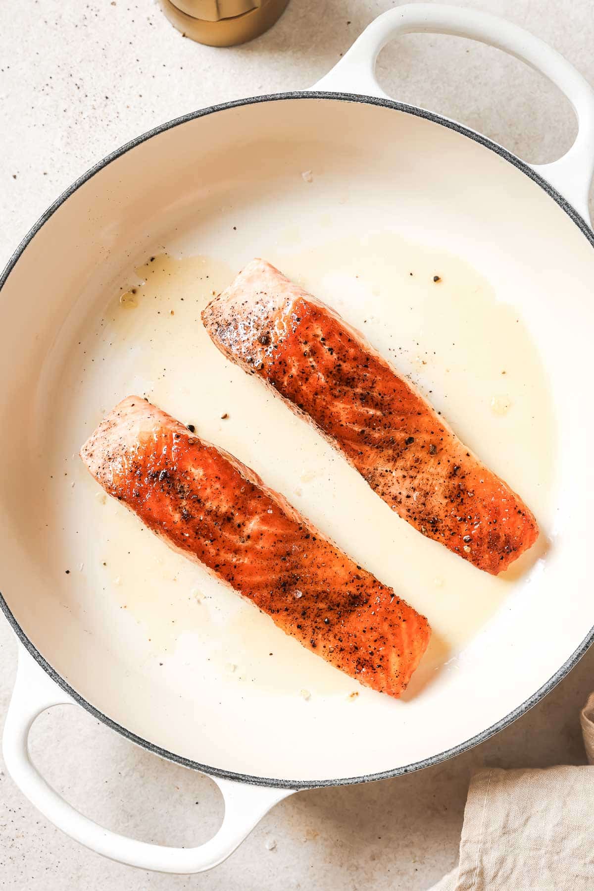 Two salmon fillets are being cooked in a skillet.