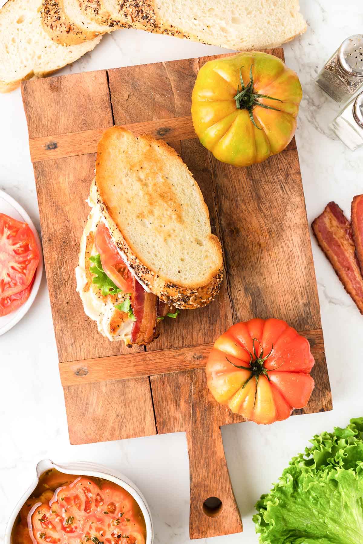 A chicken BLT sandwich on a cutting board with tomatoes, lettuce and bread.