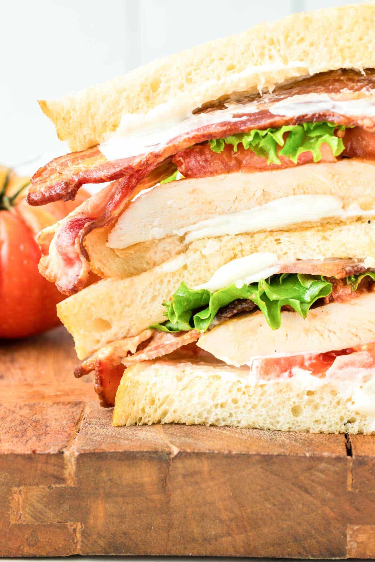 A sandwich with chicken, bacon, lettuce, and tomatoes on a wooden cutting board.