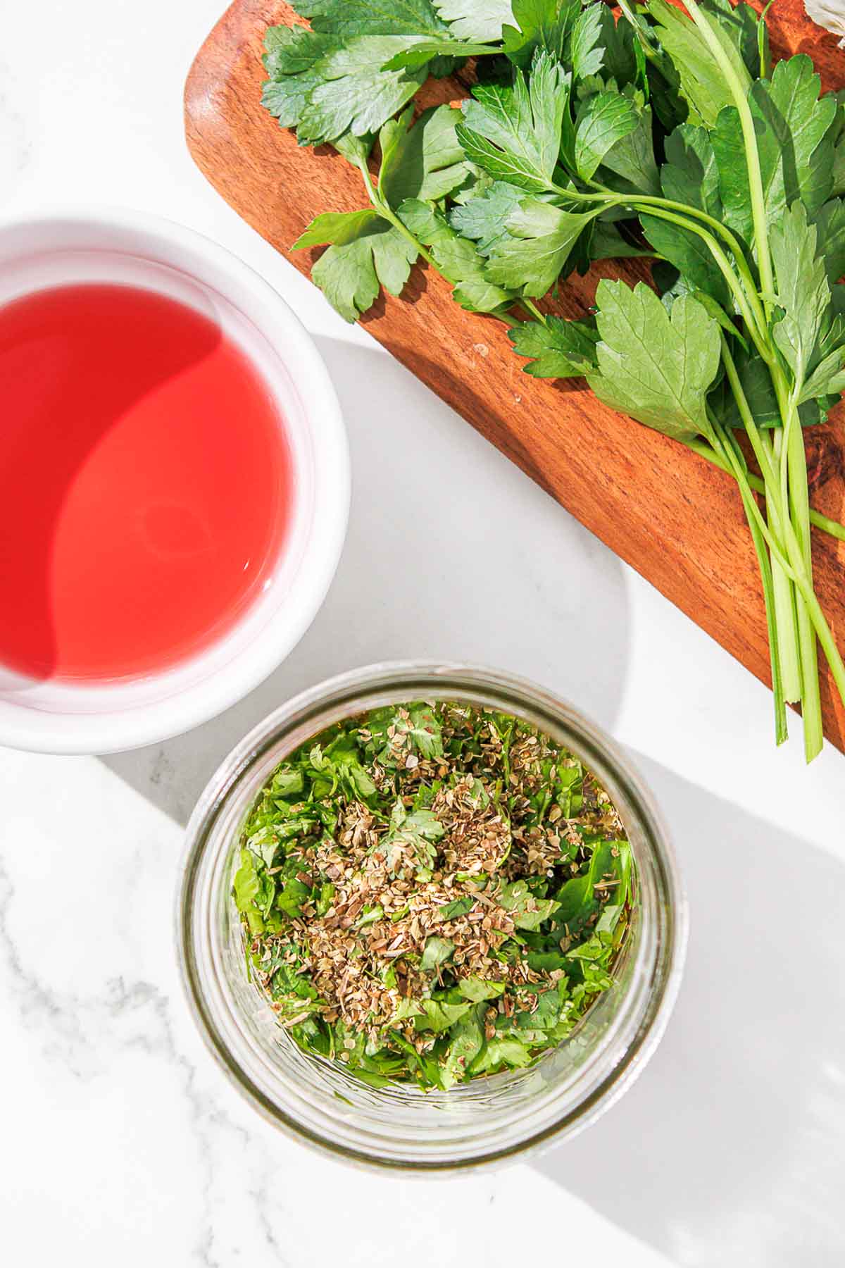 A bowl of chopped herbs and dried oregano beside a bowl of vinegar.