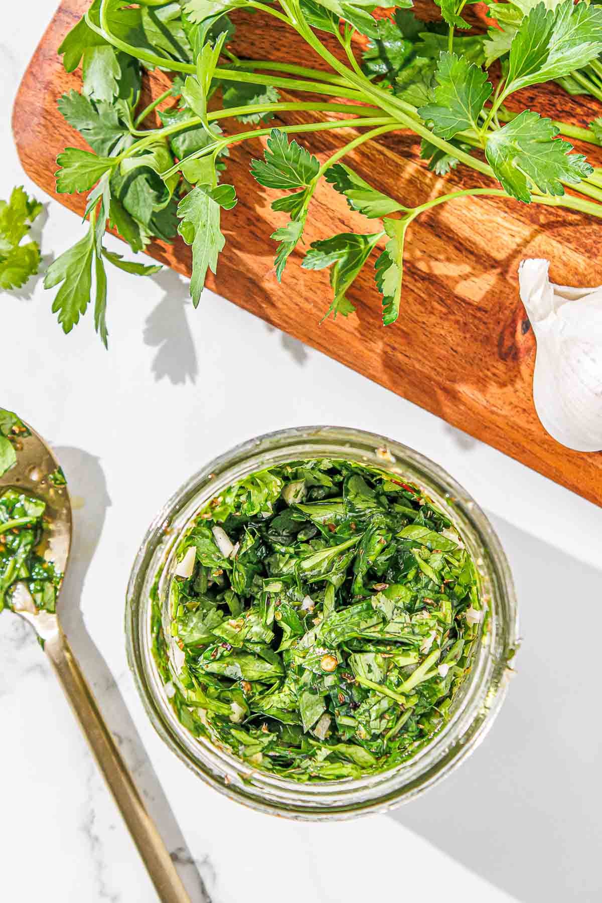 A jar of cilantro chimichurri on a wooden cutting board.