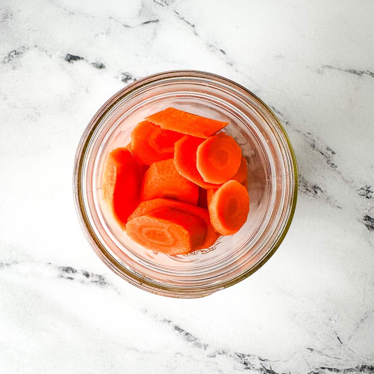 Sliced carrots in a glass jar on a marble table.