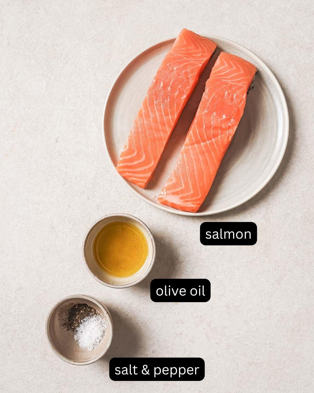 Salmon fillets with olive oil, salt, and pepper on a countertop.