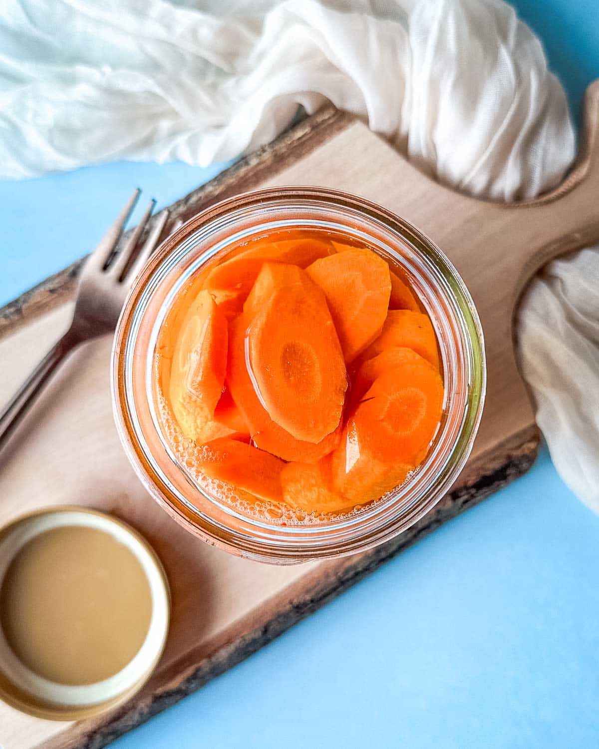 Pickled carrots in a glass jar on a wooden cutting board.