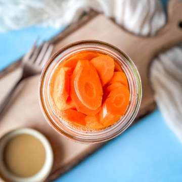 Pickled carrots in a mason jar on a blue background.
