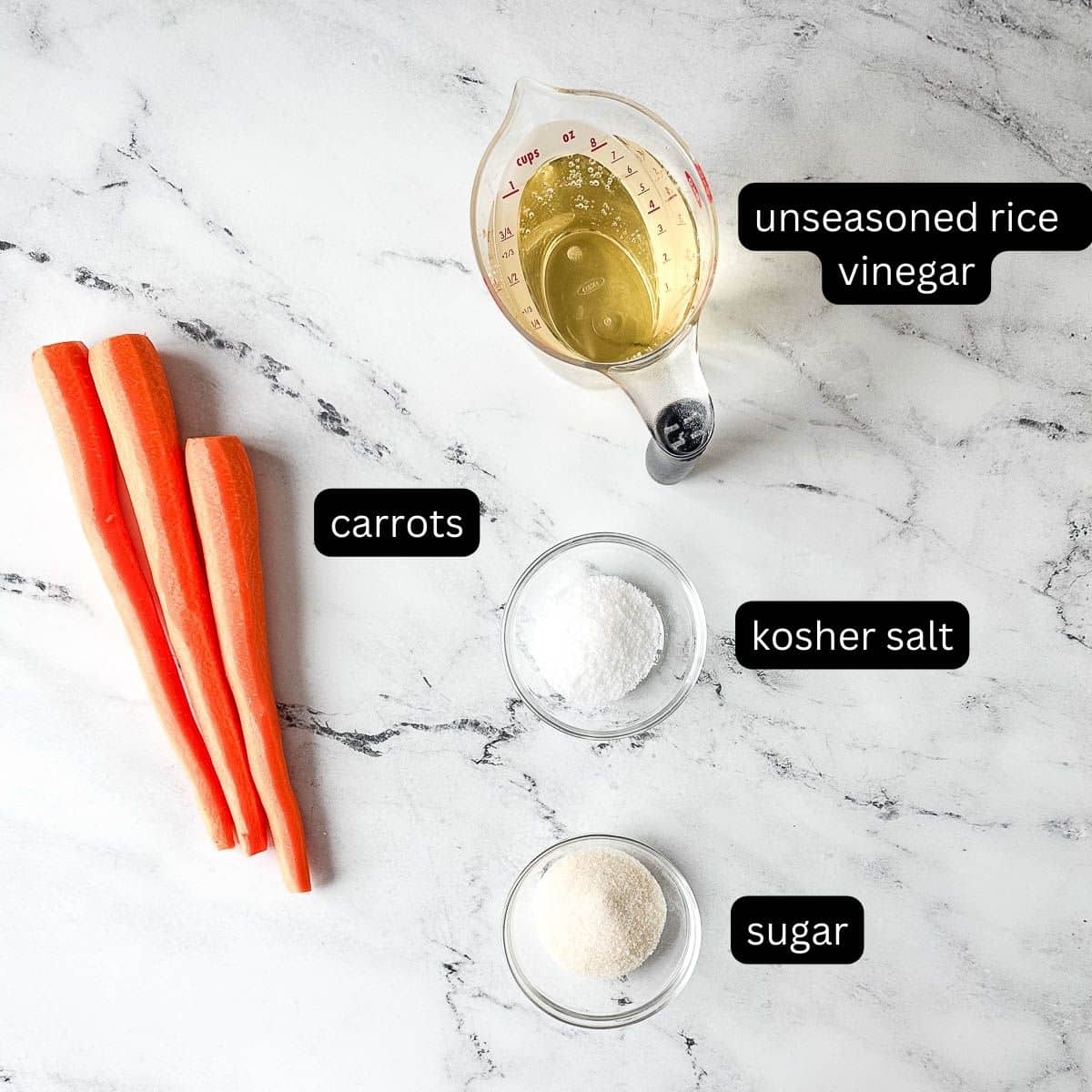 The labeled ingredients for pickled carrots are shown on a marble countertop.