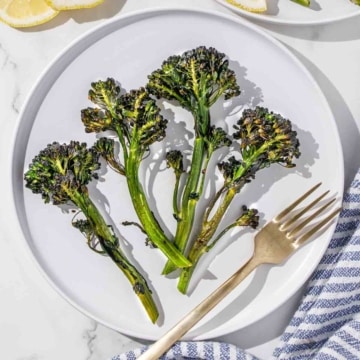 Roasted broccolini on a plate with lemon slices and a fork.